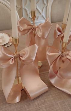 four candles with pink bows on them are sitting on a dining room table, ready to be used as centerpieces