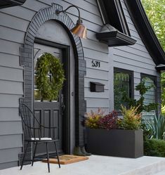 the front door of a gray house with a wreath on it and two chairs outside