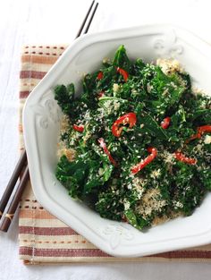 a white bowl filled with greens and red peppers on top of a striped table cloth