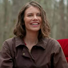 a woman sitting in a chair smiling and looking at the camera while wearing a brown shirt