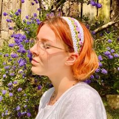 a woman with red hair wearing glasses and a headband in front of purple flowers