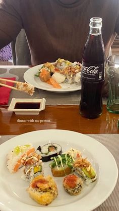 a man sitting at a table with plates of sushi and drinks in front of him