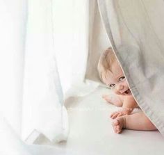 a baby is peeking out from behind a white curtain with his hands in the air