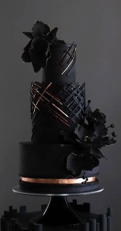 a black and gold wedding cake with flowers on top