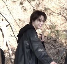 a young man holding a knife and wearing a black leather jacket while standing in front of a stone wall