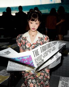 a woman sitting on the ground reading a paper with an ad in front of her