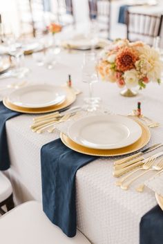 the table is set with gold and white plates, silverware, and napkins