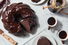 a chocolate bunt cake sitting on top of a white plate next to two cups of coffee