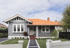 a grey house with white picket fence and trees