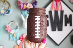 a hand holding up a glittered mason jar with a football painted on the side