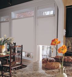 a kitchen with marble counter tops and wooden chairs next to an open window that has white roller shades on it