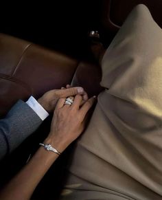 two people holding hands on top of a brown leather couch in front of a pillow