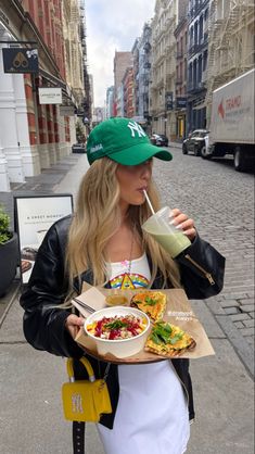 a woman is holding a tray with food and drink in her hand while walking down the street