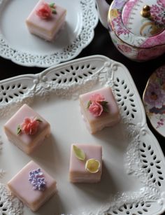 four pieces of cake sitting on a white plate next to teacups and saucers