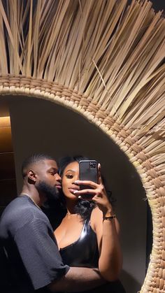 a man and woman taking a selfie in front of a straw wall with a cell phone