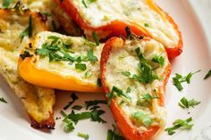 three stuffed peppers on a white plate with parsley sprinkled around them,