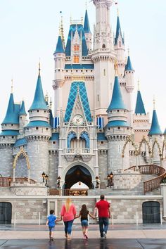 three people are walking in front of a castle with blue domes and turrets on it