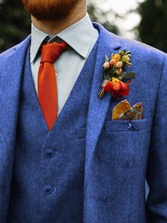 a man in a blue suit with an orange tie and flower boutonniere