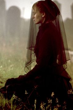 a woman sitting in the grass with a veil over her head, looking off into the distance