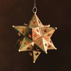 an origami star hanging from a chain on a dark background with one candle lit