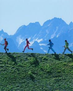 four people are running up a hill with mountains in the background