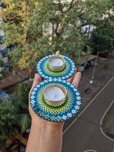 a hand holding two tea cups and saucers on top of each other with trees in the background