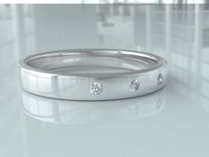 a wedding band with three diamond stones on the inside and outside, sitting on a shiny surface