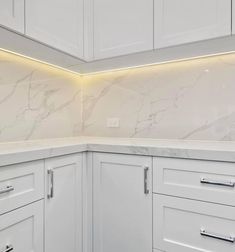 a kitchen with white cabinets and marble counter tops, along with an under cabinet lighting