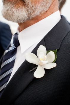 a man wearing a suit and tie with a white flower on it's lapel