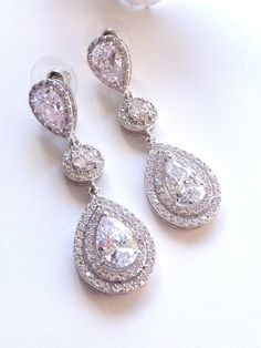 This earring features a white gold plated clear white teardrop cubic zirconia surrounded by 2 layers of little cubic zirconia gems (about 60 gems around it),  dangle from a white gold plated halo round cubic zirconia and a LARGE pear shaped cubic zirconia post earrings. Size: 5.3 (L) x 1.8  (W) cm or 2.1(L)  x 0.72  (W) inches long. Matching Bracelet and Necklace: https://www.etsy.com/listing/225770378/bridal-bracelet-double-halo-round-rose Note: The pear shaped post stud earring used in this design is sightly larger than my other design which has the similar post earrings. If it is a larger pear shaped post stud used, I will mentioned it as large in the listing and the title. **NOTE: CUBIC ZIRCONIA HAS MANY DIFFERENT GRADES, AND ALL THE CUBIC ZIRCONIA USED IN MY DESIGN IS OF THE HIGHEST Q Diamond Teardrop Chandelier Earrings, Dazzling White Teardrop Crystal Earrings, Dazzling Diamond White Teardrop Chandelier Earrings, Dazzling Diamond White Teardrop Crystal Earrings, Dazzling Teardrop Crystal Earrings In Diamond White, Teardrop Chandelier Earrings With Diamond Accents, White Cubic Zirconia Teardrop Earrings For Party, Cubic Zirconia Drop Chandelier Earrings, Diamond White Teardrop Bridal Earrings