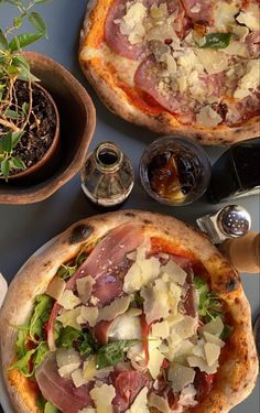 two pizzas with different toppings sitting on top of a table next to plants