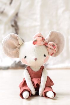 a small stuffed animal with a pink bow on its head sitting on the floor in front of a white wall