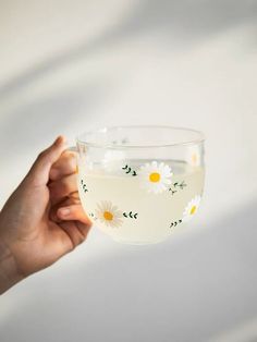 a hand holding a glass filled with water and daisies on the inside of it