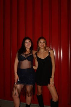 two young women standing next to each other in front of a red wall wearing black clothing