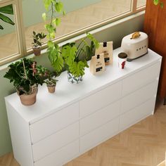 a white dresser with plants on it in front of a window