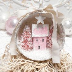 a small pink house with a star on top in a white cloth covered basket next to ornaments