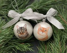 two ornaments with cats painted on them hanging from a tree