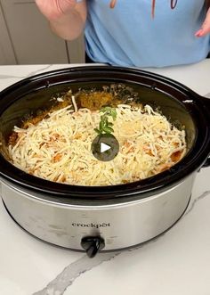 a woman holding her hands up in front of a slow cooker filled with food