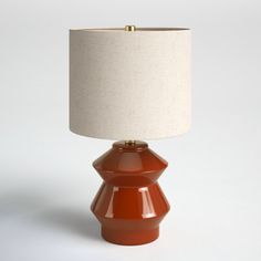 an orange table lamp with a white shade on the base and a beige linen lampshade