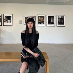 a woman sitting on top of a wooden bench in front of some pictures hanging on the wall