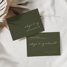 two green business cards sitting on top of a white sheet with feathers in the background