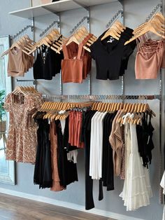 a rack with clothes hanging on it in a clothing store next to a wall mounted mirror