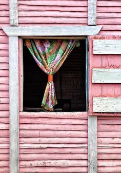 an open window on the side of a pink building with curtains hanging from it's sides