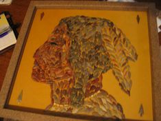 a painting with leaves on it sitting on top of a wooden table next to a pen and paper