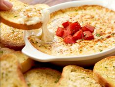 a person dipping cheese into a bowl of dip with toasted bread on the side