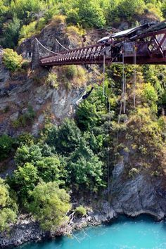 a man is suspended from a bridge over a river in the middle of a forest