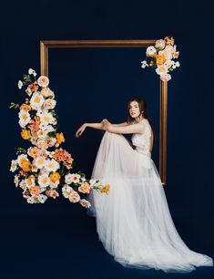 a woman is posing in front of a frame with flowers on it and holding her arm out