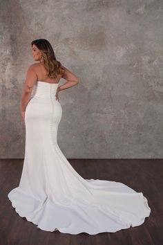 a woman in a white wedding dress standing on a wooden floor with her back to the camera