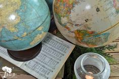 two globes sitting on top of an open book next to a candle and some music sheets