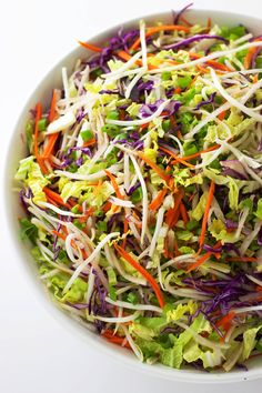 a white bowl filled with shredded carrots, cabbage and sprouts on top of a table